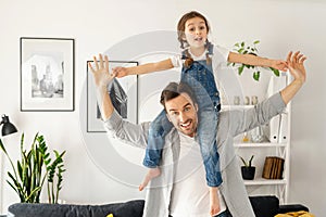 Cute girl spreading arms pretends plane and smiles. Loving father carrying his little toddler daughter on the shoulders