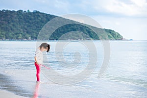 Cute girl stand and watched the sea water splashing at his feet on the sandy beach. Child looked excitedly at her feet.