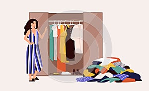 Cute girl standing in front of opened wardrobe with apparel hanging inside and pile of clothes on floor. Concept of photo