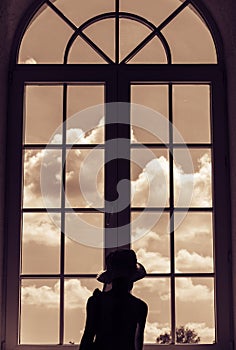 Cute girl stands near a window and looks at the sky with clouds