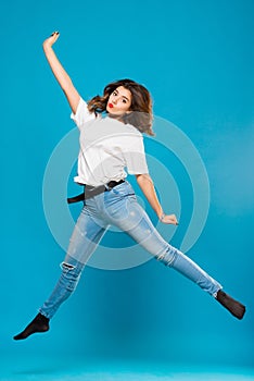 Cute girl student teenager jumping waving hands on a blue background. The concept of happiness, carefree and positive