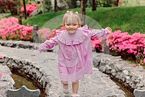 Cute girl in stylish dress playing in summer garden with pink flowers