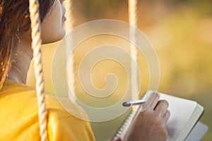 Cute girl on  swing with a notebook and pen keeps a diary of feelings in nature, a woman composes and writes, romantic mood