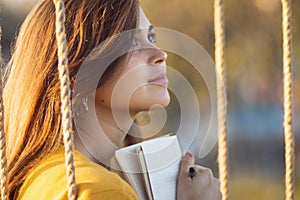 cute girl on a swing with notebook and pen keeps a diary of feelings in nature, a woman composes and writes, romantic mood