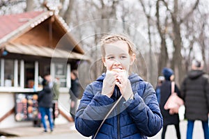 A cute girl takes a bite of a pie bought in a food truck in a city park in early spring. Takeaway food