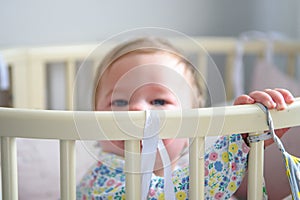 Cute girl of ten months old, playing alone in a crib at home in the afternoon or in the morning.