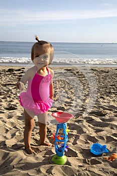 Cute girl toddler on the beach playing in sand with toys