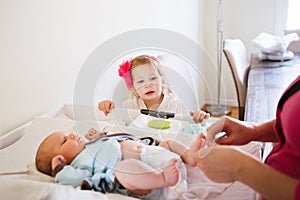 Cute girl toddler helping her mother, changing baby diaper