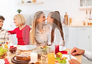 Cute girl touching noses with mom at festive table, celebrating family holiday together with her nears at home