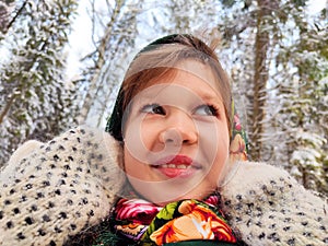 Cute girl in a traditional Russian headscarf and mittens on winter forest. Closeup portrait of a child in folk clothes