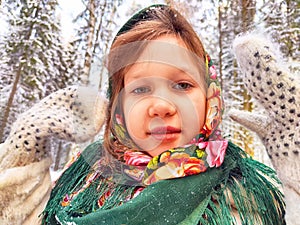 Cute girl in a traditional Russian headscarf and mittens on winter forest. Closeup portrait of a child in folk clothes