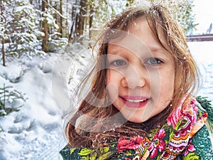 Cute girl in a traditional Russian headscarf and mittens on winter forest. Closeup portrait of a child in folk clothes