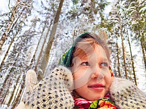 Cute girl in a traditional Russian headscarf and mittens on winter forest. Closeup portrait of a child in folk clothes