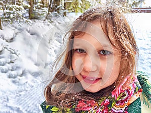 Cute girl in a traditional Russian headscarf and mittens on winter forest. Closeup portrait of a child in folk clothes