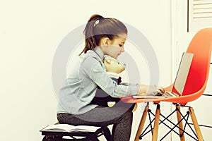 Cute girl typing on laptop with teddy bear toy