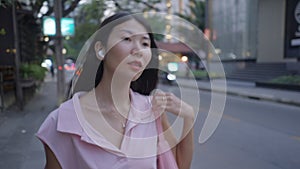 Cute girl walking happily on the street with headphones on her ear and a bag on her shoulder