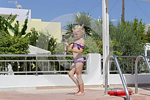 A cute girl walks along the pool on a clear sunny day. Holding goggles in his hands