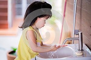 Cute girl is washing her hands with soap at the white sink. Asian child clean their palms after playing.