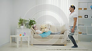 Cute girl is waving magic wand, and daddy in funny clothes is obying her commands, jumping.