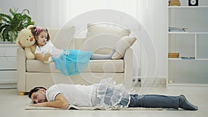 Cute girl is waving magic wand, and daddy in funny clothes is obying her commands, lying on the floor, completely tired.