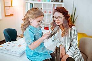 Cute girl wearing denim dress and glasses using calculator sitting near mom