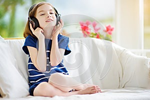 Cute girl wearing huge wireless headphones. Pretty child listening to the music. Schoolgirl having fun listening to kid`s songs at