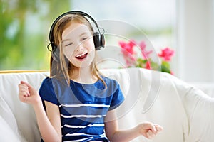 Cute girl wearing huge wireless headphones. Pretty child listening to the music. Schoolgirl having fun listening to kid`s songs at