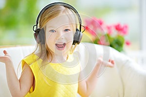 Cute girl wearing huge wireless headphones. Pretty child listening to the music. Schoolgirl having fun listening to kid`s songs at