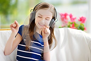 Cute girl wearing huge wireless headphones. Pretty child listening to the music. Schoolgirl having fun listening to kid`s songs at