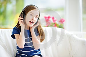 Cute girl wearing huge wireless headphones. Pretty child listening to the music. Schoolgirl having fun listening to kid`s songs at