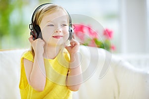 Cute girl wearing huge wireless headphones. Pretty child listening to the music. Schoolgirl having fun listening to kid`s songs at