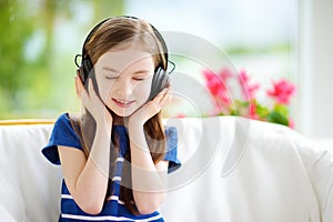 Cute girl wearing huge wireless headphones. Pretty child listening to the music. Schoolgirl having fun listening to kid`s songs at