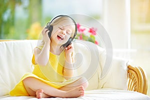 Cute girl wearing huge wireless headphones. Pretty child listening to the music. Schoolgirl having fun listening to kid`s songs at