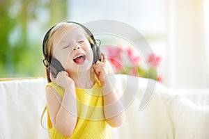 Cute girl wearing huge wireless headphones. Pretty child listening to the music. Schoolgirl having fun listening to kid`s songs at