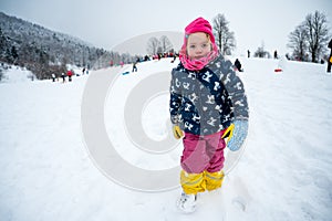 Cute girl wearing pink hat posing on snowy slope.