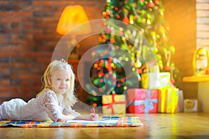 Cute girl in a white dress lies on the floor and writes a letter to Santa.