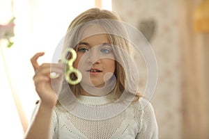 Cute girl in white shirt playing with green fidget spinner in bright room