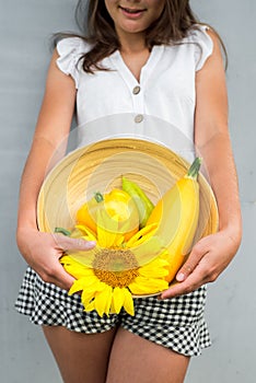 Cute girl wit autumn harvest at the wall. Harvesting, yellow sunflower, pepper and pumpkin