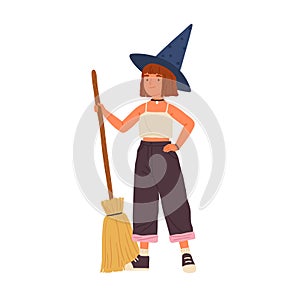 Cute girl in witch hat standing with a broomstick. Portrait of funny little wizard or sorcerer holding magic broom
