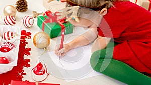 Cute girl writing letter to Santa on livingroom floor. Young girl writing her christmas wishlist.