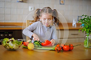 Cute girl of younger school age cuts vegetables and greens for salad.