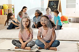 Cute girls sitting on floor while kindergarten teacher reading book to other children