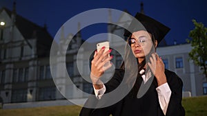 Cute graduate girl preening using her phone.