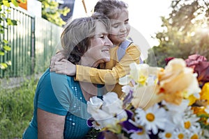 Cute granddaughter hugging her happy grandmother. The hugs of an elderly woman and a little girl against the backdrop of summer