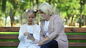 Cute granddaughter teaching granny how to use modern smartphone, generation gap