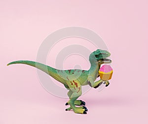 Cute green plastic dinosaur toy with cupcake decorated pastel pink background