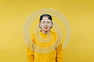 Cute guy in a cap and casual clothes isolated on a yellow background, looking at the camera and smiling