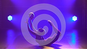 Cute gymnast performs elements of rhythmic gymnastics with ball. Girl dressed in burgundy body sportsuit n a dark studio