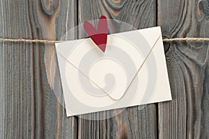 Cute handmade white paper envelope with red heart as stamp, hanging on rope on dark wooden background. Secret present