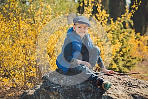 Cute handsome boy in stylish blue dress and hat close to yellow flowers enjoying spring time